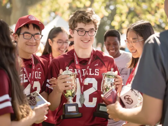 A group of smug-looking students wearing Stanford jerseys, holding trophies and shaking hands with famous alumni.