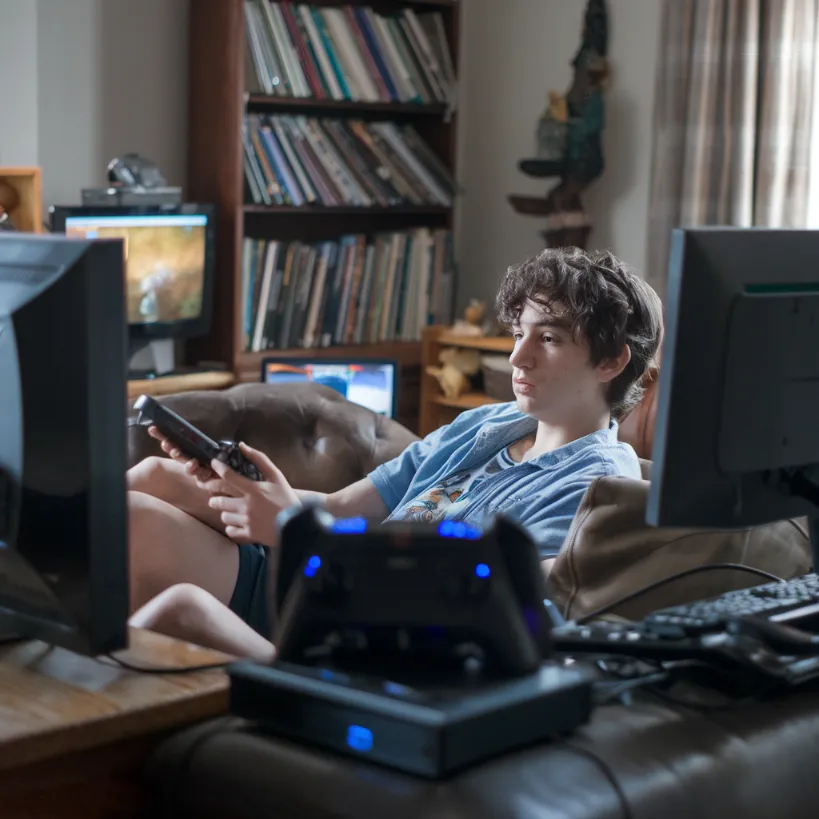 Nielsen ratings outdated metrics, A "rare photograph" of a young person in their natural habitat, surrounded by multiple streaming devices, captured by bewildered Nielsen researchers using a long-range lens